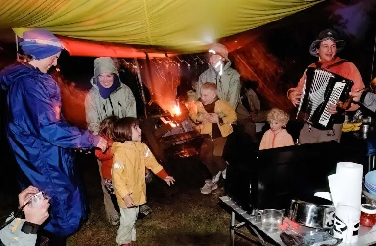 Family camping under a tarp playing music and dancing