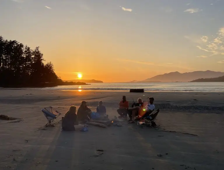 sunset photo over a beach with people sitting around a fire