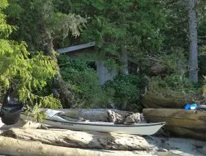 2 kayaks on a beach with a cabin and forest behind