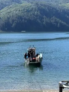 Motorboat with people on a calm blue lake, forested mountains in the background and a dock in the foreground