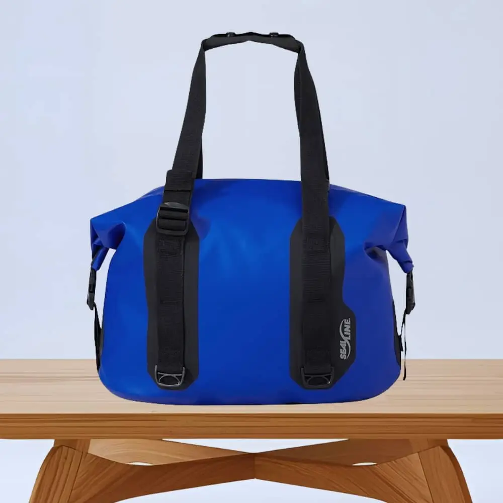 Blue waterproof duffel bag with two black adjustable straps on a wooden table.